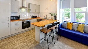 A modern kitchen with white cabinets, a wooden countertop, and a blue sofa with yellow cushions.