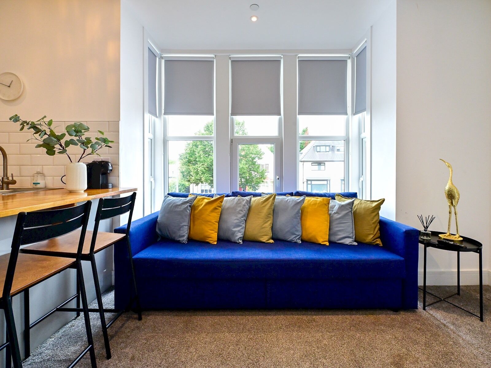 A modern living room with a blue sofa, black chairs, a coffee machine, and a view of the outside.