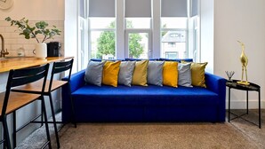 A modern living room with a blue sofa, black chairs, a coffee machine, and a view of the outside.