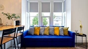 A modern living room with a blue sofa, black chairs, a coffee machine, and a view of the outside.
