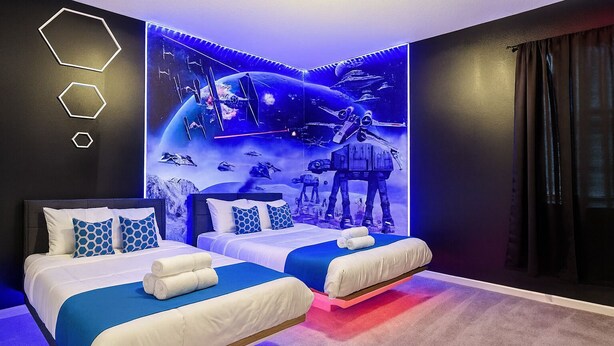 A modern hotel room with two beds, a large wall mural of space-themed artwork, and a dark color scheme.