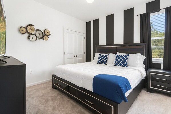 Un dormitorio con cama, mesitas de noche, cómoda, puerta y decoración en las paredes.