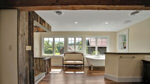 A spacious room with a wooden floor, a large window, a chair, and a bathtub. - The Farmhouse at Pine Creek (Watson Township)
