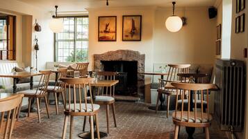 A cozy restaurant with brick flooring, wooden tables and chairs, a fireplace, and artwork on the walls.