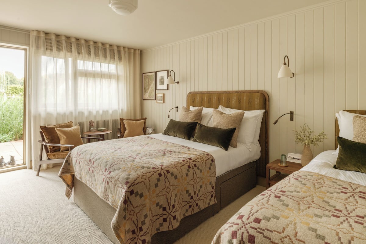 Ein Hotelzimmer mit einem großen Bett, einem Sessel, einem kleinen Tisch und einem Nachttisch mit einer Lampe.