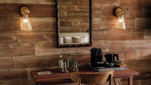 A rustic wooden room with a wooden desk, a chair, a mirror, and two wall-mounted lamps. - The Royal George (Tintern)