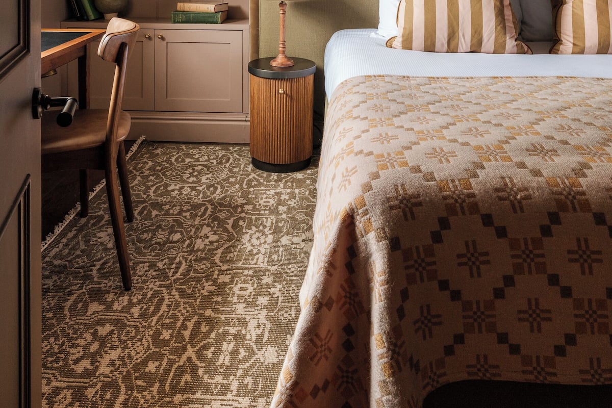 Ein Schlafzimmer mit schrägen Wänden, einem Bett mit gestreiften Kissen, einem Nachttisch mit Lampe und einem kleinen Regal mit Büchern und Pflanzen.