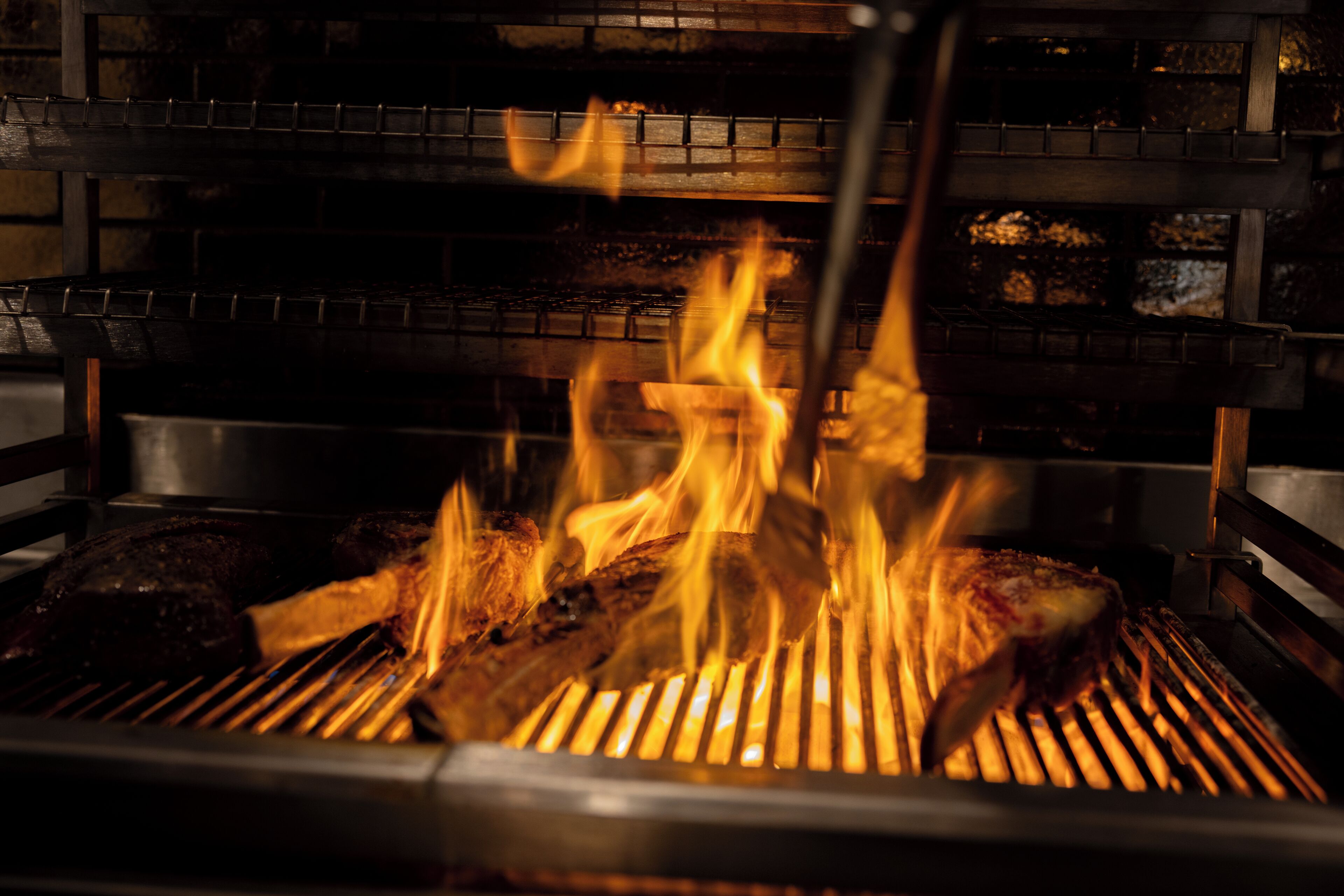 A grill with flames, a metal rack, and a brick wall in the background.