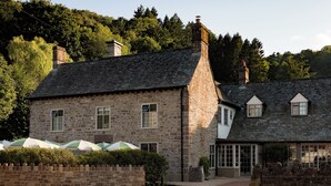 A stone building with a steeply pitched roof, large windows, and a stone wall with a gate. - The Royal George (Tintern)