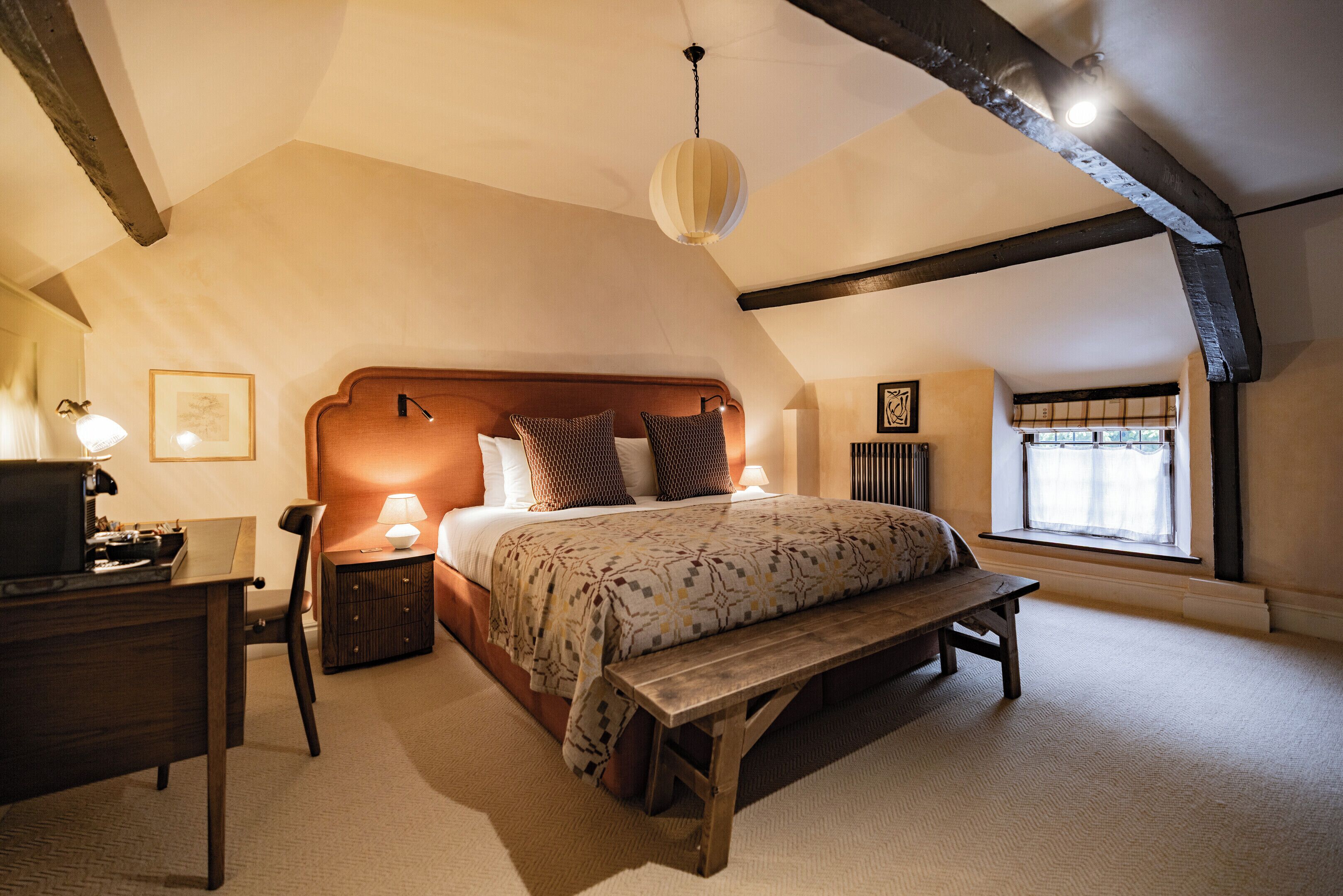 A bedroom with a wooden bed, a bench, a desk, and a window with a view.