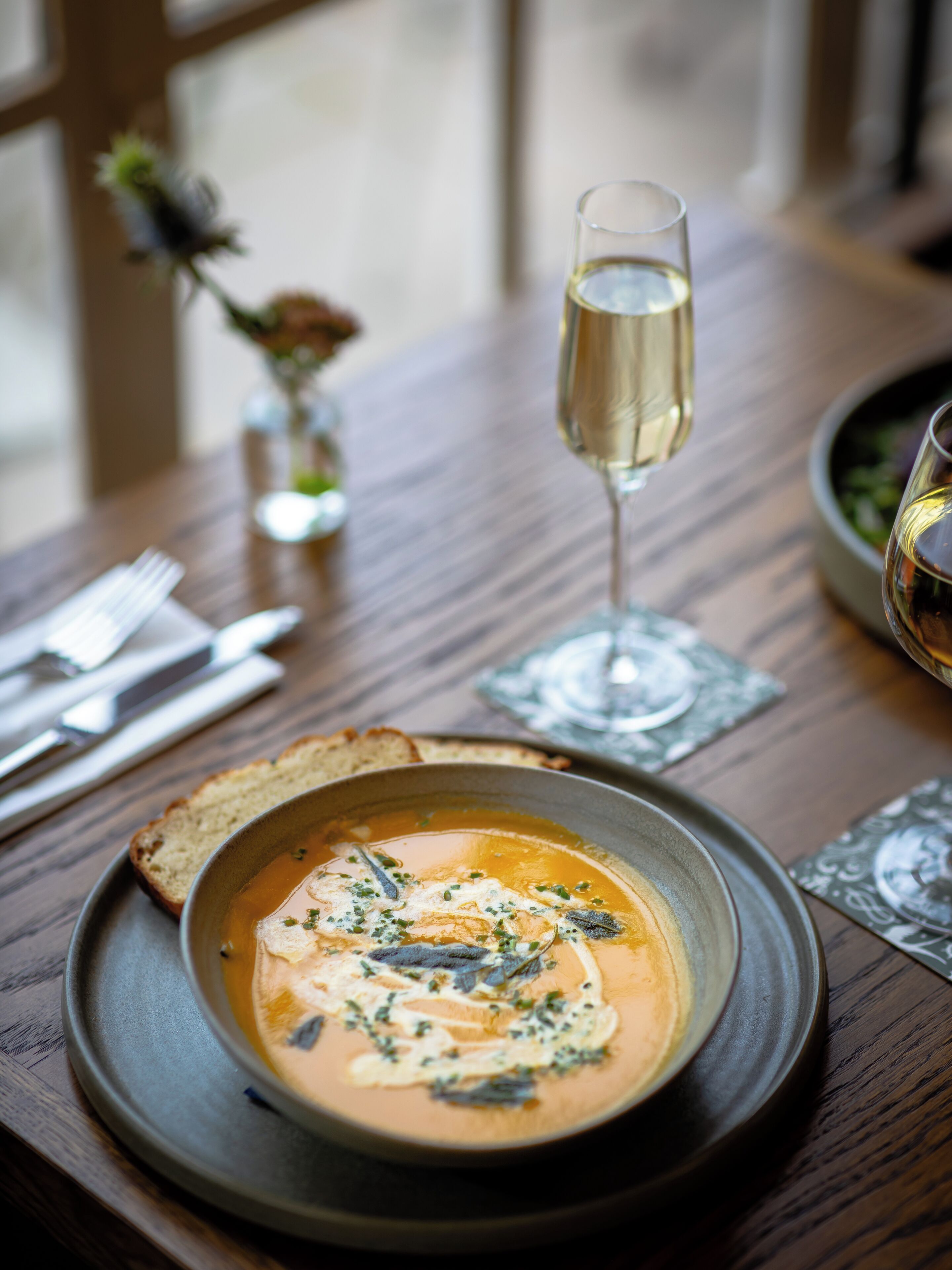A dining table with a bowl of soup, a glass of wine, and a vase with flowers.
