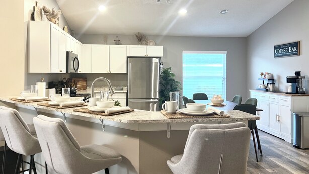 A modern kitchen with a central island, white cabinetry, stainless steel appliances, and a coffee bar sign. - 4BR Private Pool & Spa | Game Room | 35 Min to Disney (Davenport)