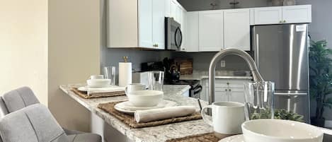 A modern kitchen with white cabinets, a stainless steel refrigerator, and a granite countertop.