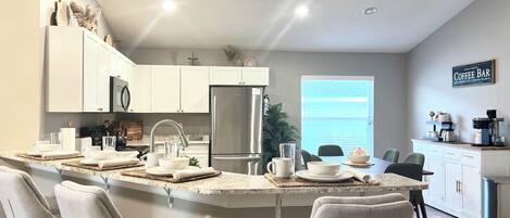 A modern kitchen with a central island, stainless steel appliances, and a coffee bar sign.