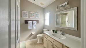 A bathroom with a white sink, beige cabinets, a large mirror, and three framed pictures on the wall.