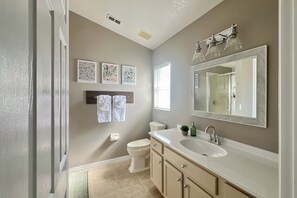 Un baño con un lavamanos blanco, armarios color beige, un espejo grande y tres cuadros en la pared.