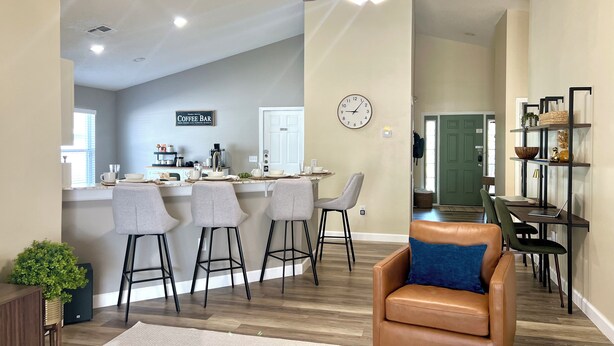 A modern kitchen with a bar area, a dining area with a laptop, and a living room with a leather sofa.