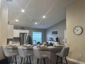 A modern kitchen with a central island, bar stools, a refrigerator, and a clock on the wall.