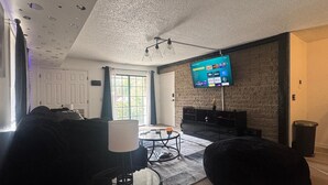 Ein modernes Wohnzimmer mit einem an einer Ziegelwand montierten Flachbildfernseher, einem schwarzen Sofa, einem Glastisch und einem schwarzen Sitzsack.