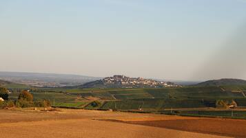 Un paysage rural avec des vignobles, un village perché sur une colline et, au loin, des collines ondulantes.