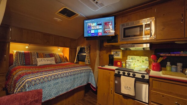 A cozy RV interior with a bed, kitchenette, and a mounted TV displaying streaming services. - Edith - Glamping in Springs Country. Walk to downtown High Springs! (High Springs)