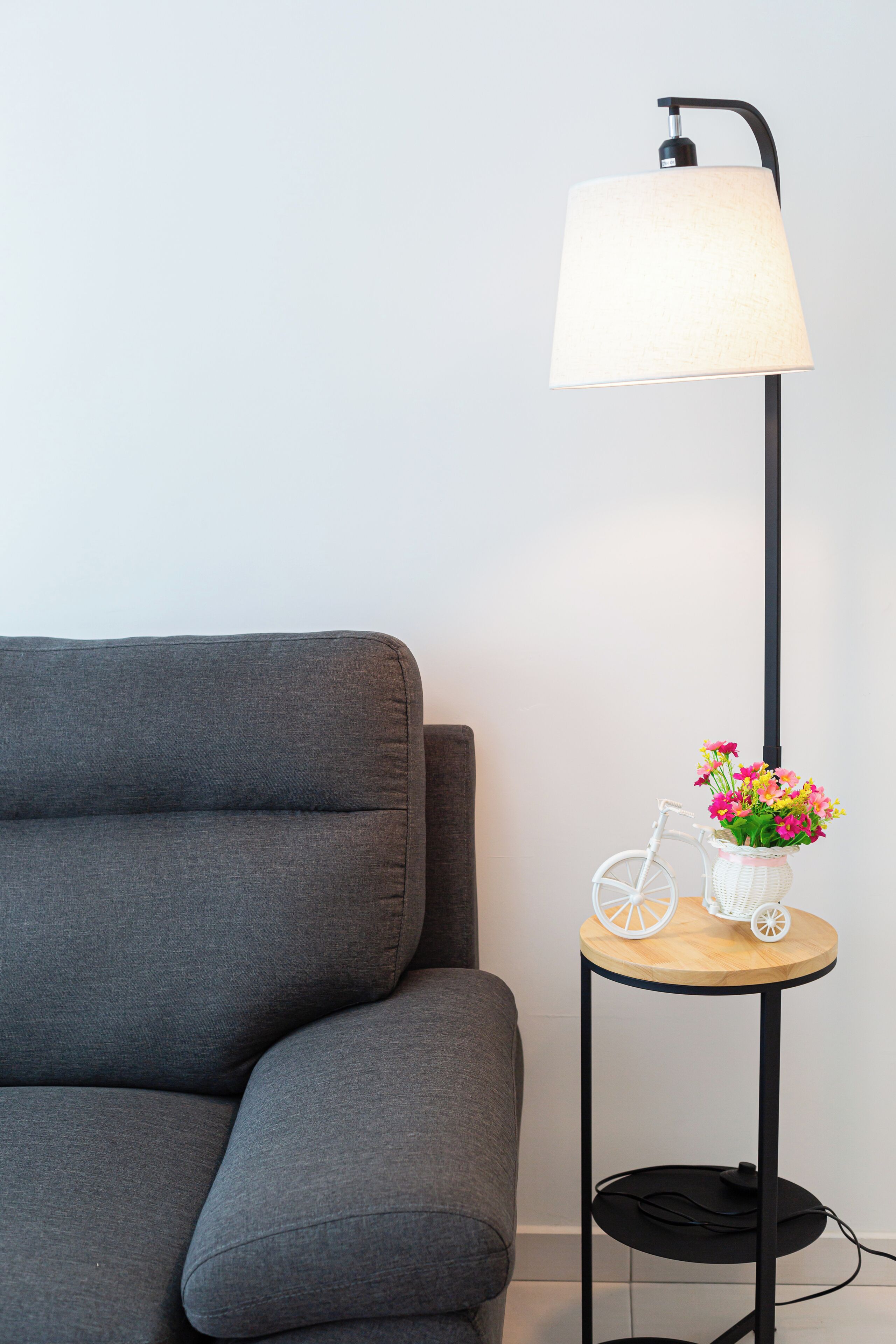 A grey sofa, a floor lamp, and a small table with a white bicycle and flowers.