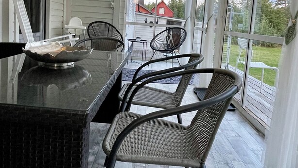 Eine überdachte Terrasse mit Essbereich, ausgestattet mit Tisch und Stühlen, einer Glaseinfriedung und Blick ins Freie.