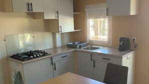 A compact kitchen with white cabinets, a gas stove, a sink, and a coffee maker. - Renovated mobile home bathroom with Italian shower (Gavaudun)