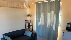 A small, cozy room with a wooden table, a dark blue sofa, a small cabinet, and a curtain. - Renovated mobile home bathroom with Italian shower (Gavaudun)