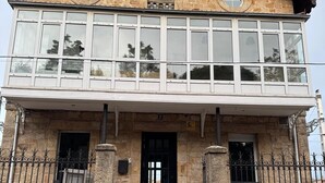 Un edificio de piedra de dos pisos, con un balcón, una puerta negra y una escalera que conduce a la entrada.