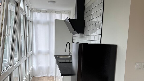 Una cocina moderna con un refrigerador negro, armarios blancos y una ventana con cortina.