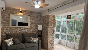 Una habitación con pared de piedra, ventilador de techo, ventana grande y un sofá gris con cojines estampados.