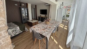 Un espacio habitable moderno con comedor, sofá, televisión y área de cocina.