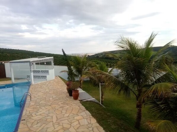 A swimming pool with a stone pathway, a covered seating area, and palm trees.