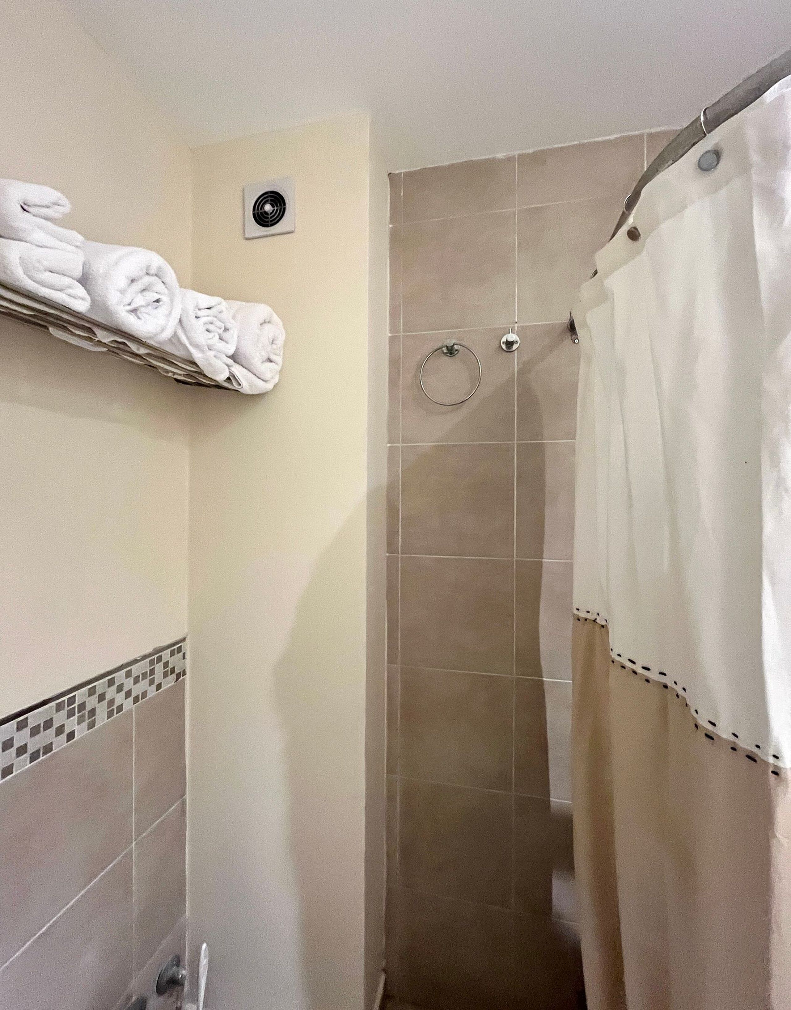 Une salle de bain avec un rideau de douche, un porte-serviettes avec des serviettes pliées et un ventilateur fixé au mur.