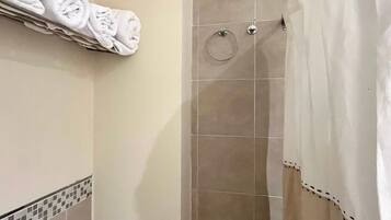 Une salle de bain avec un rideau de douche, un porte-serviettes avec des serviettes pliées et un ventilateur fixé au mur.