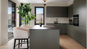 Une cuisine moderne dotée d’un îlot central, de meubles de rangement aux couleurs sombres et d’une grande fenêtre.