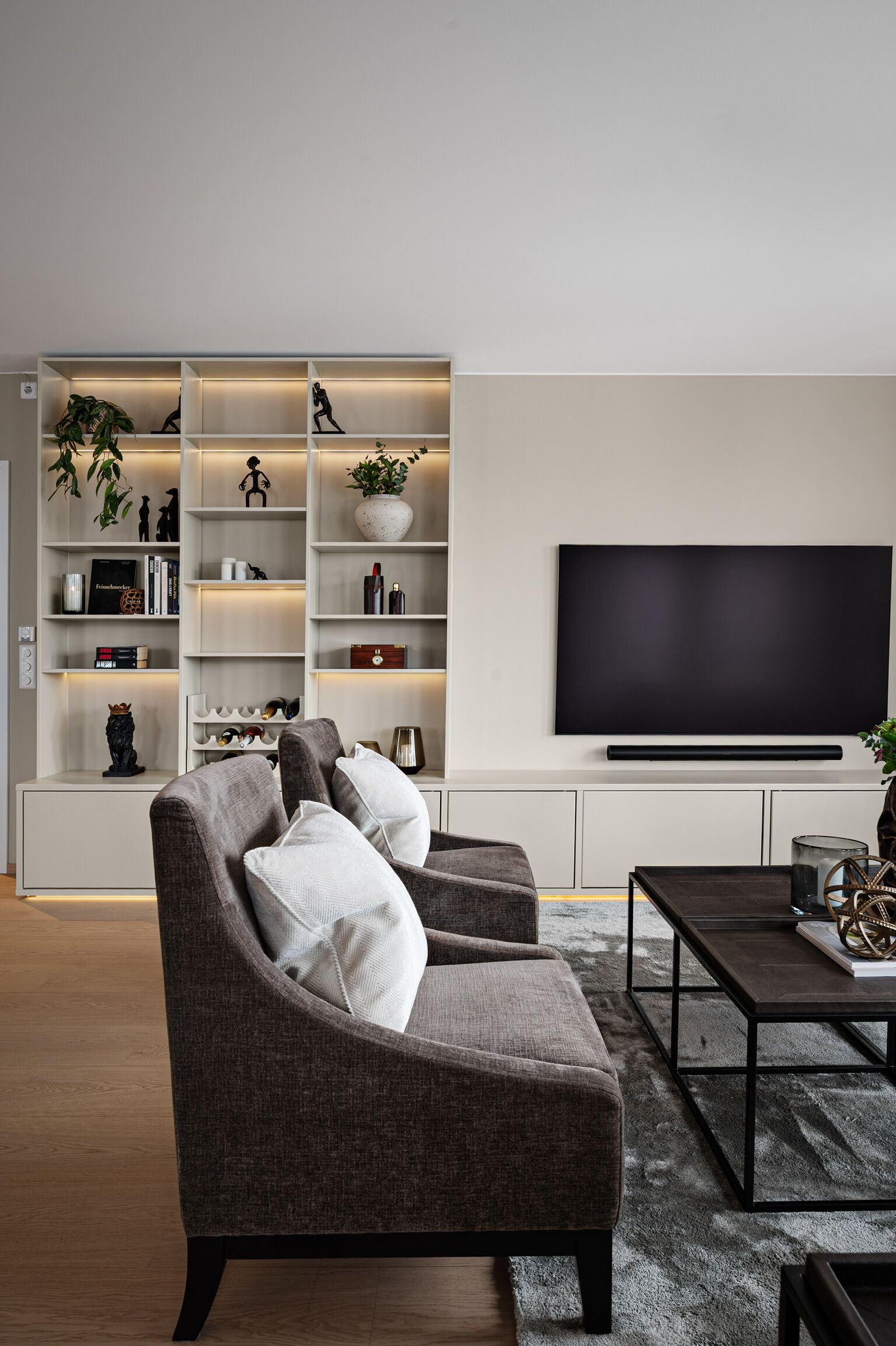 A modern living room with a grey sofa, a flat-screen TV, and a built-in bookshelf with decorative items.