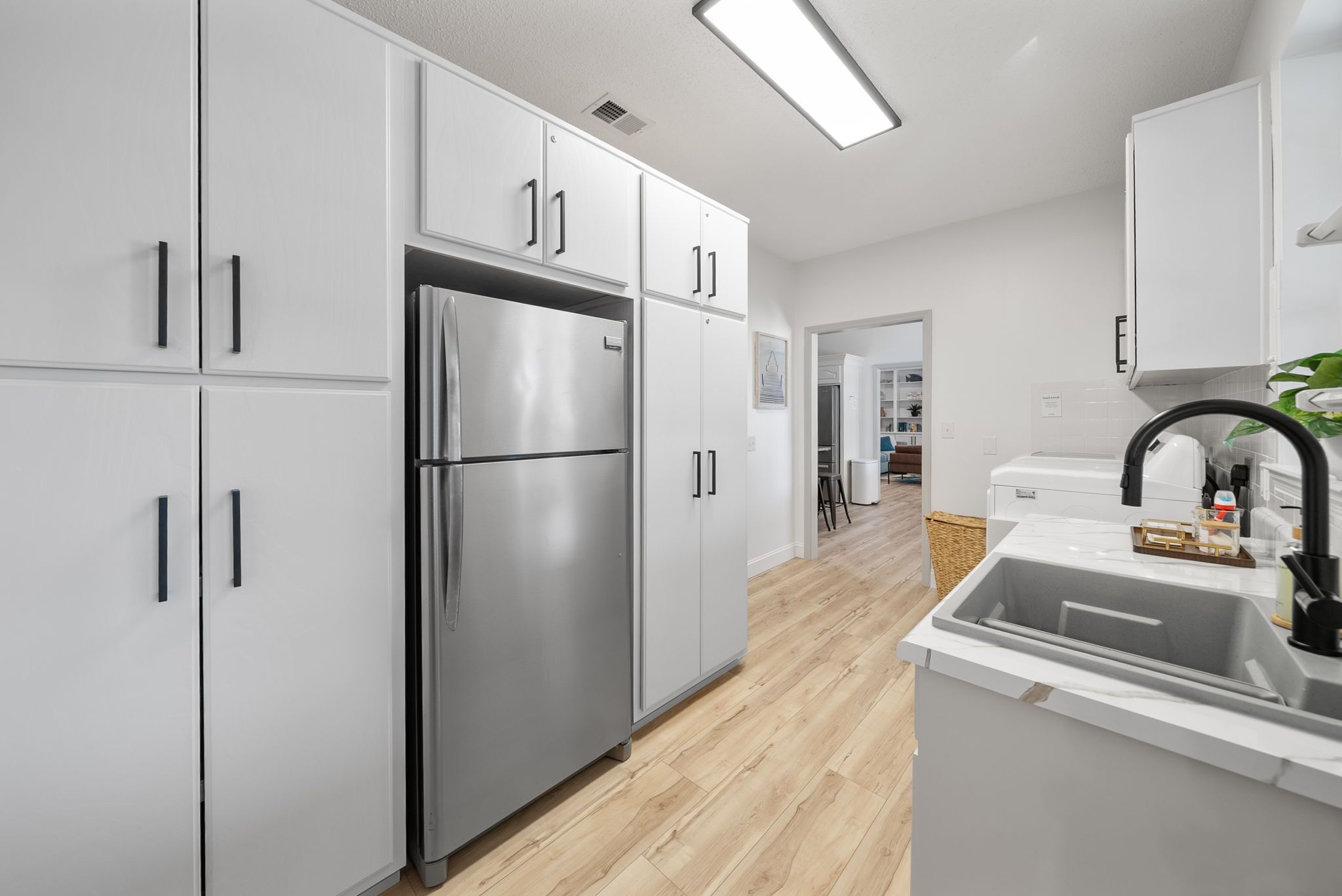 Una cocina moderna con armarios blancos, un refrigerador de acero inoxidable y un lavamanos con grifo negro.