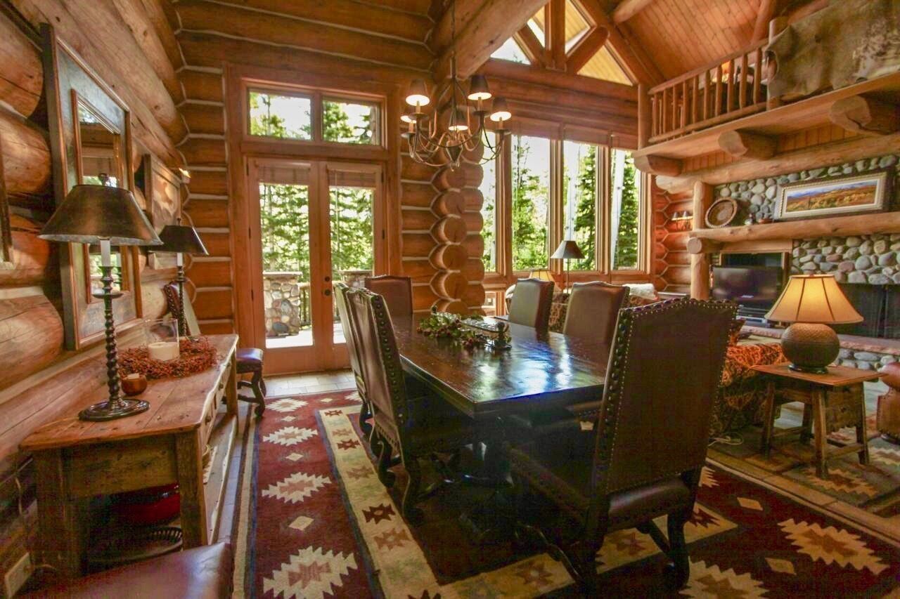 A log cabin interior with a dining table, chairs, a fireplace, and a large window.