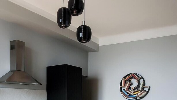 A modern kitchen with a central island, bar stools, a black cabinet, and a unique wall art piece. - Comfortable newly renovated room Isola/Dergano area (Milano)
