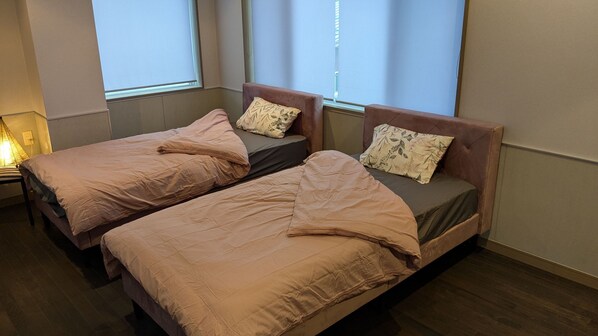 Two single beds with matching headboards and pillows, a bedside table, and a window with blinds.