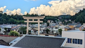 A view of a traditional Japanese torii gate, residential buildings, and a mountainous landscape.