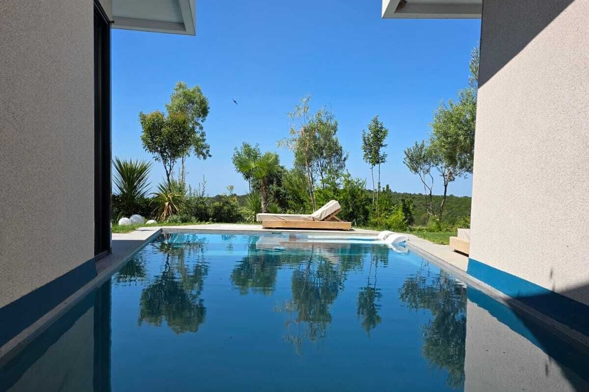 A modern pool with clear blue water, surrounded by lush greenery and a clear sky.