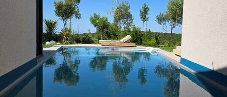 A modern pool with clear blue water, surrounded by lush greenery and a clear sky.