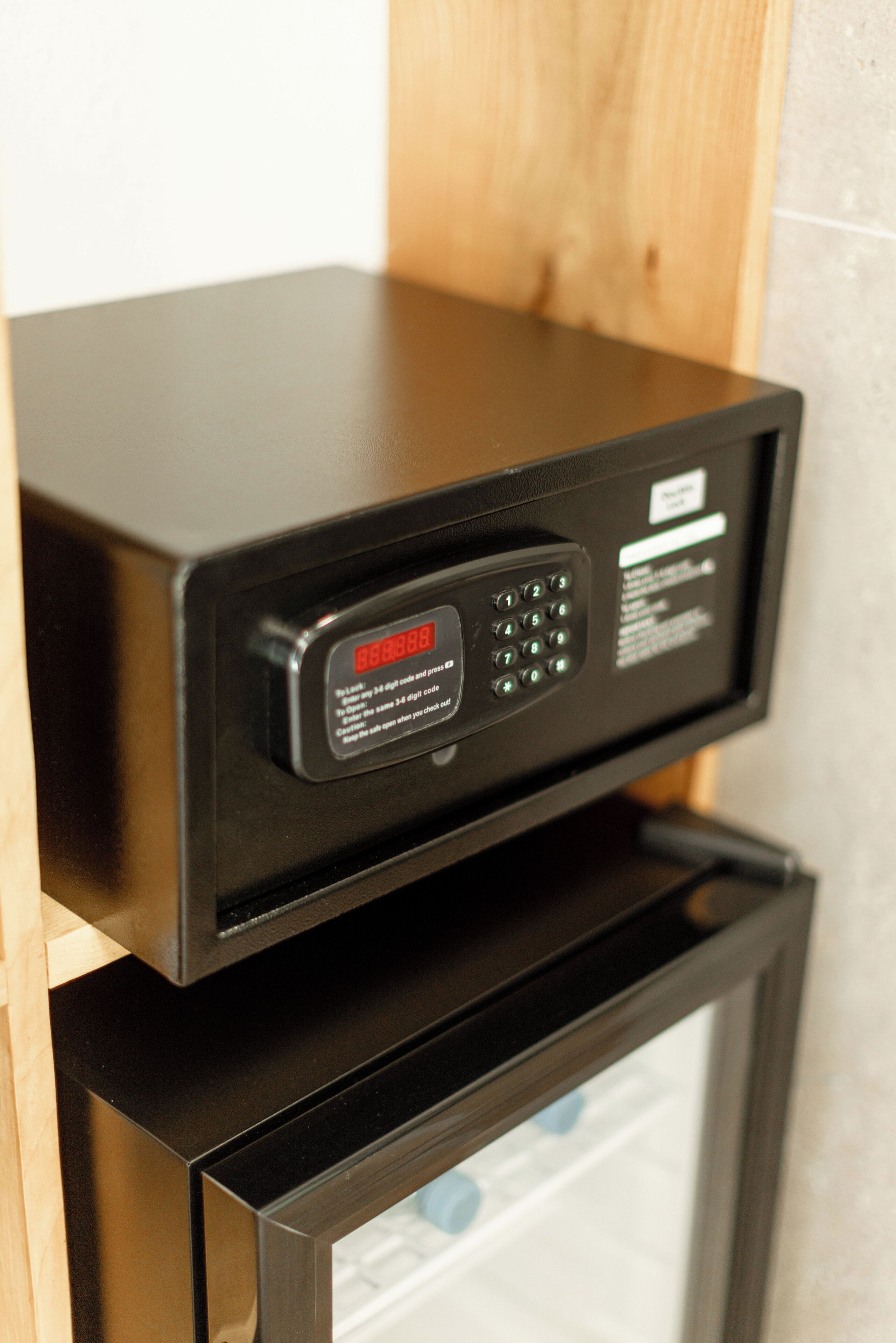 A black microwave oven with a digital display and keypad, placed on a wooden shelf above a glass door.