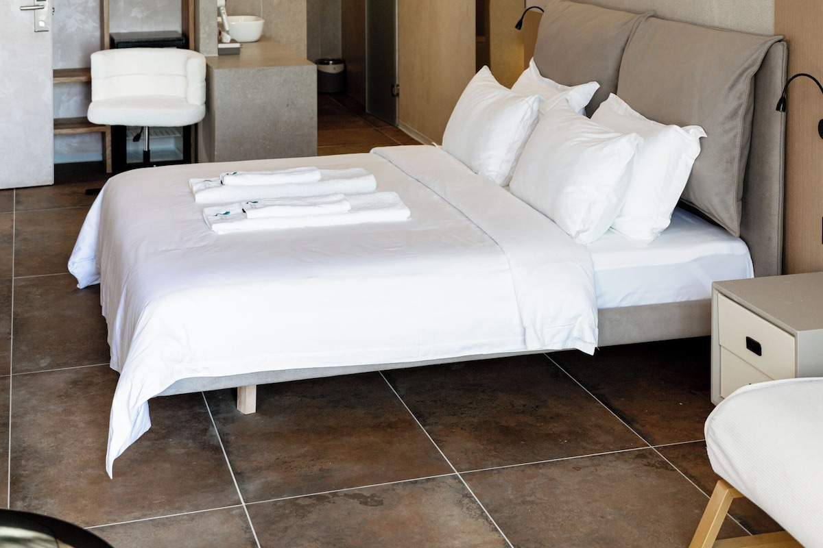A modern hotel room with a large bed, a bedside table, a chair, and a bathroom visible through an open door.
