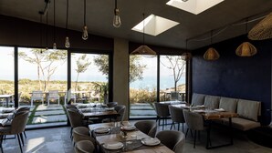 A restaurant with large windows, tables set for dining, and hanging light fixtures. - Cape of Rodon Resort Green Village (Ishëm)