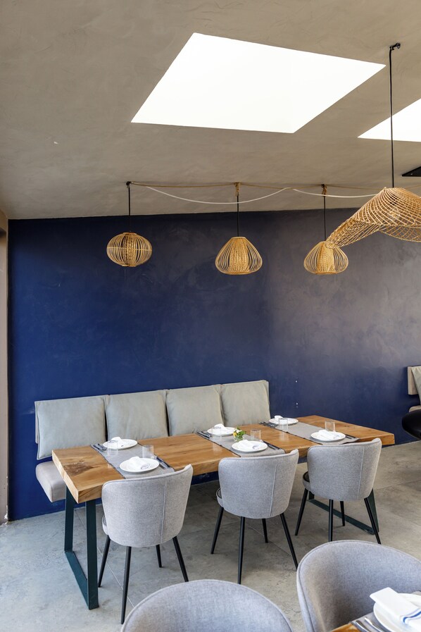 A modern dining area with a wooden table, grey chairs, and a blue accent wall. - Cape of Rodon Resort Green Village (Ishëm)