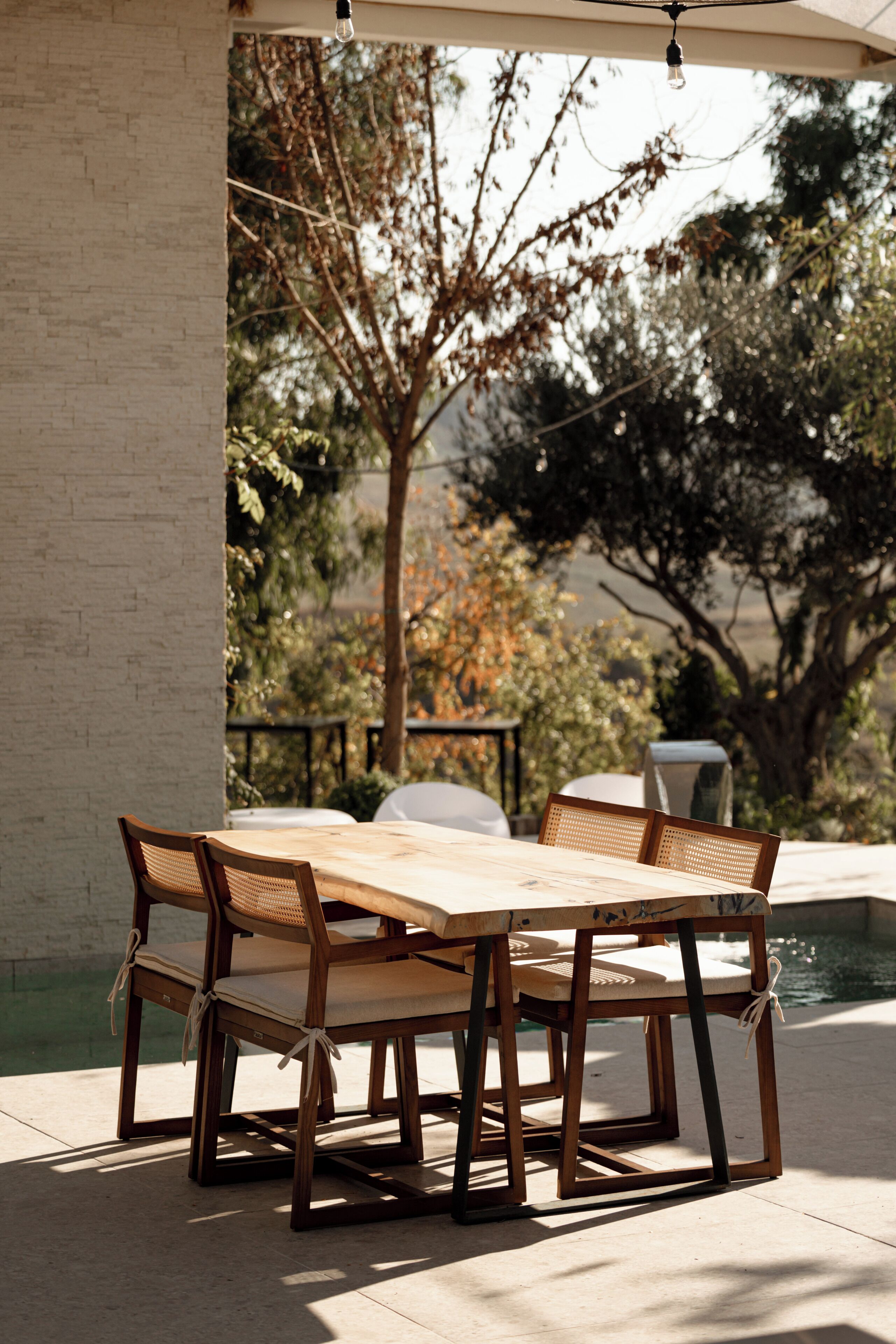 Une table et des chaises en bois sont disposées à l’extérieur, avec une piscine en arrière-plan.
